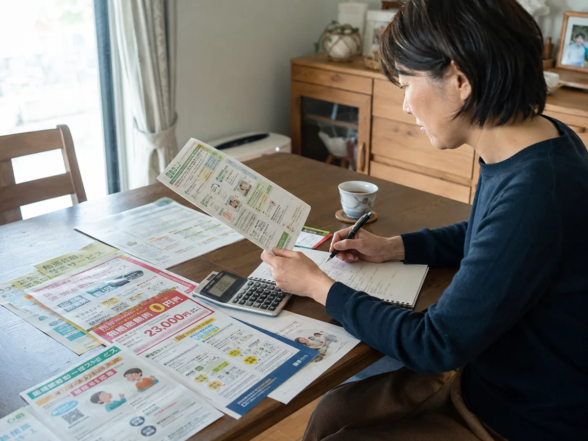 電卓と複数のサービス資料で買い物支援の費用を比較検討する女性