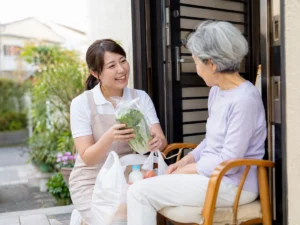 エプロン姿の支援スタッフが買い物の野菜を見せながら高齢女性と話す